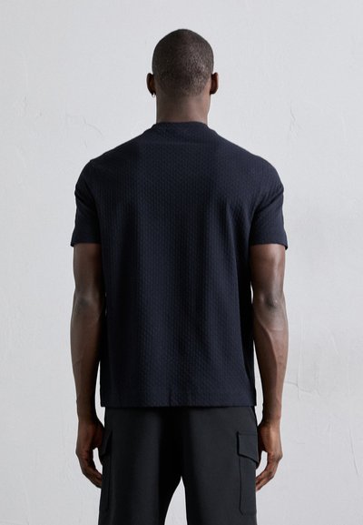 Σαλοπέτα ναυτικού χρώματος με υφή, κοντομάνικη μπλούζα σε ευθεία γραμμή, με στρογγυλή λαιμόκοψη και διακριτικό σχέδιο, συνδυασμένη με μαύρες cargo βερμούδες.