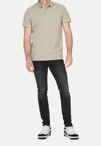 Beige polo shirt met contrasterende kraag en mouwafwerking, gecombineerd met donkere jeans en zwart-witte sneakers. Heeft een klein logo op de borst.