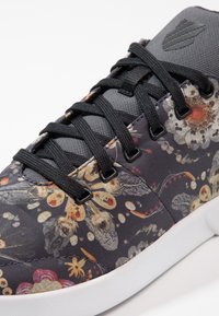 Chaussure de sport à motif floral avec une tige en tissu noir, des lacets noirs et une semelle en caoutchouc blanche à finition texturée.