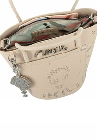 Hellbeige Bucket Bag mit perforiertem Muster, silbernem Zubehör und einem Anhänger. Enthält ein gefüttertes Innenleben aus gemustertem Stoff und mehrere Fächer.