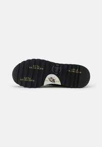 Melnas gumijas zoles ar dziļiem protektoriem; iekļauj reljefus tekstus un logotipa akcentus dzeltenā un baltā krāsā. Izturīga, teksturēta virsma labākai saķerei.