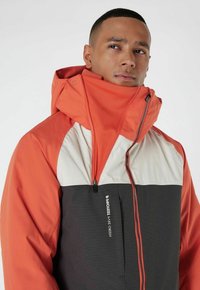 Wasserabweisende Jacke mit einem Farbkombinationsdesign in Orange, Weiß und Grau, hohem Kragen und Reißverschluss, der mit einem Logo-Detail an der Tasche versehen ist.