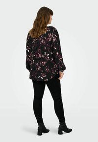 Črna cvetna bluza z vijoličastimi in belimi detajli, dolgimi rokavi in sproščenim krojem, v kombinaciji z črnimi ozkimi kavbojkami in gležnjarji.