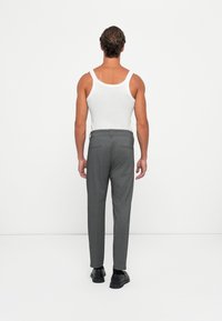 Pantaloni grigi su misura con taglio dritto, texture sottile e due tasche posteriori. Indossati con un top bianco e scarpe nere.