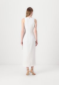 Rochie lungă albă fără mâneci, cu o silueta ajustată, închidere cu fermoar pe spate și o fanta în partea de jos. Purta sandale cu toc înalt, nude.