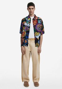 Short-sleeve, multicolored patterned shirt with vibrant graphics; paired with beige wide-leg pants and brown slip-on shoes.
