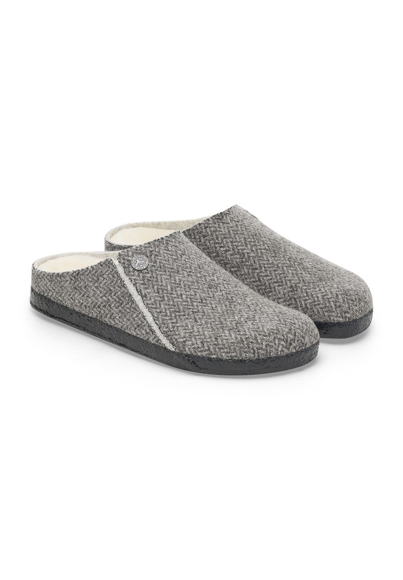 Chaussons en laine gris avec un motif en chevrons, doublure intérieure douce et semelle en caoutchouc noire. Présente un emblème décoratif sur un côté.