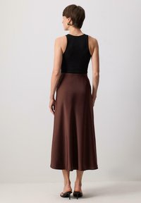 Débardeur noir ajusté associé à une jupe midi fluide en satin marron, présentant une texture lisse et un léger éclat, ainsi que des chaussures noires à talons hauts.