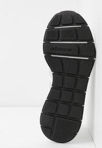 Zwarte rubberen sneakerzool met gestructureerde grippatronen en een reliëf Adidas-logo. Platte vormgeving met rechthoekige profiel elementen.