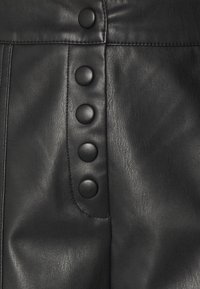 Tessuto in pelle nera con una texture liscia e cuciture ben evidenti, con sei grandi bottoni neri come dettagli notevoli lungo un lato.