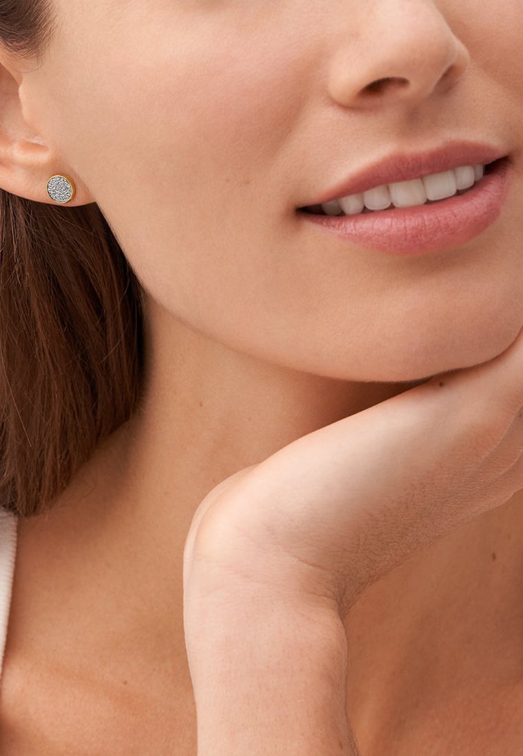 Boucles d'oreilles à clou en ton or, arborant un design circulaire texturé, se détachant sur un fond neutre, mettant en valeur l'éclat du matériau.