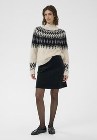 Sweter dziany w kolorze kremowym z czarnym i szarym geometrycznym wzorem, sparowany z czarną spódnicą z kordurowej tkaniny. Czarne buty i przezroczyste czarne rajstopy.