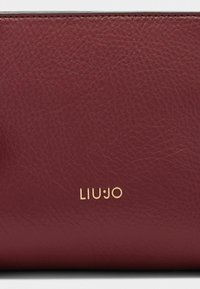 Borsa in pelle bordeaux con superficie texturizzata e logo dorato "LIU∙JO". Il design è rettangolare con linee pulite e accenti minimali.
