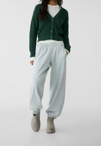 Green knitted cardigan with buttons, layered over a white top, paired with light gray sweatpants featuring elastic cuffs and beige ankle boots.