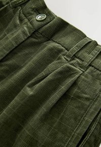 Pantaloni din catifea verde, cu un model texturat, închidere cu nasture și pliuri pe față pentru un plus de detaliu și design.