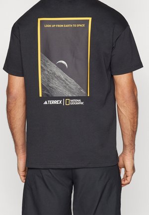 T-shirt noir affichant un graphisme sur le thème de l'espace avec la Terre se levant au-dessus d'une surface rocheuse et un texte indiquant "LOOK UP FROM EARTH TO SPACE."