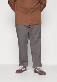 Bruine short-sleeve shirt gecombineerd met grijze broek en bordeauxrode sneakers met witte strepen. Ontspannen pasvorm met een soepele textuur.