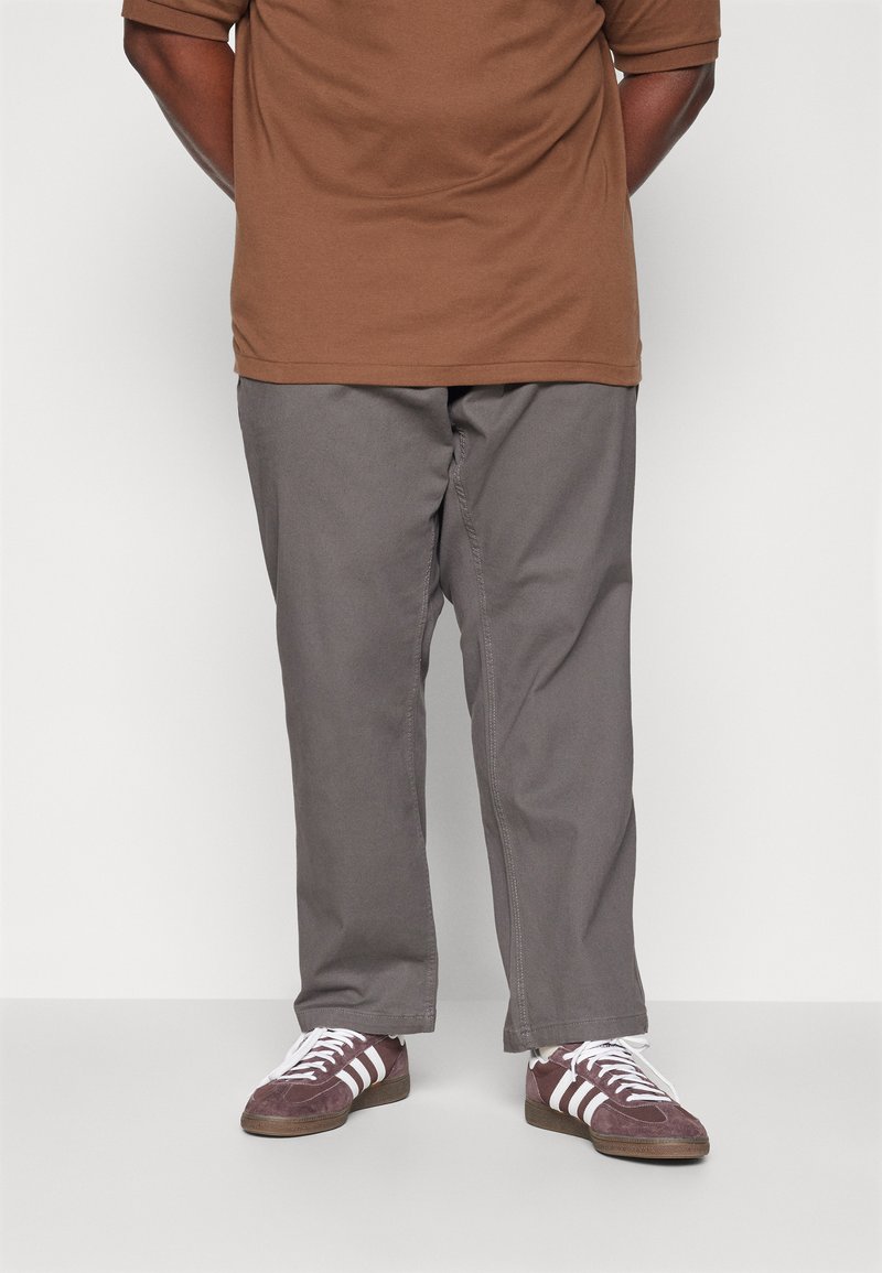Bruine short-sleeve shirt gecombineerd met grijze broek en bordeauxrode sneakers met witte strepen. Ontspannen pasvorm met een soepele textuur.