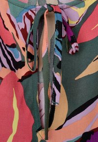 Barevná květinová látka má velké růžové a zelené vzory. Stahovaný výstřih přidává texturu, látka je vyrobena z jemné a lehké bavlny.