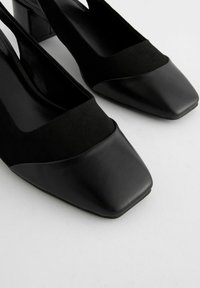 Mustat slingback-korkokengät, joissa on pehmeä mokkanahka päällinen, neliön muotoinen kärki ja lohkokorko. Muotoilu yhdistää mattapintaisia ja sileitä nahkatekstuureja.