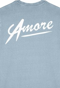 Ljusblå t-shirt med stor vit kursiv text "Amore" över den övre delen av ryggen, med en mjuk bomullstextur.