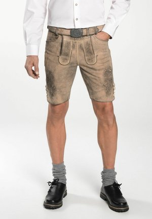 Lederhorts mit floraler Prägung, beige Farbe, taillierte Passform, zwei Vorderpockets und dekorativen Knöpfen. Kombiniert mit schwarzen Schuhen und grauen Socken.