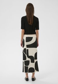 Schwarzes, geripptes Kurzarm-Oberteil kombiniert mit einem cremefarbenen Midirock mit markanten schwarzen geometrischen Mustern. Glatte Textur und figurbetonte Silhouette.