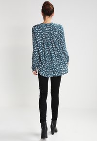 Långärmad turkos blus med ett tryckt vitt djurmönster, som har en plisserad bakdel och är kombinerad med svarta slim fit byxor och ankelstövlar.