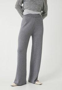 Grå vidde bukser lavet af blødt stof, med høj talje og diskrete slidser i kanten, parret med en grå sweater.