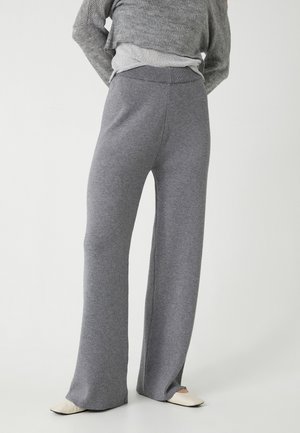 Pantalones de pierna ancha grises, fabricados con un material suave, cuentan con una cintura alta y leves aberturas en los dobladillos, combinados con un suéter gris.