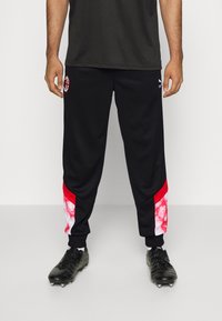 Svarta träningbyxor med en tight passform, med röda accenter och ett tie-dye-mönster på de nedre sidorna. Logotypen visas på låret.