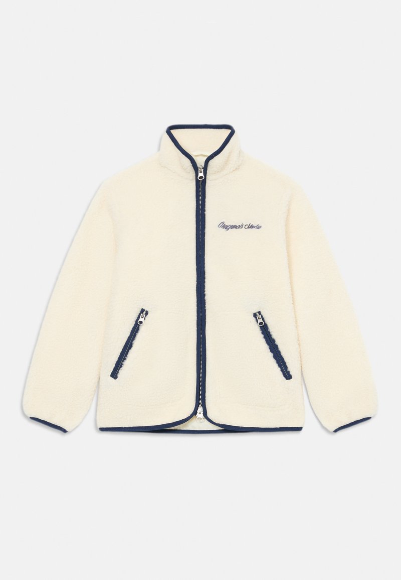 Bunda iz flisa v kremni barvi s temno modrim robom; zadrga spredaj, visok ovratnik in dve stranski žepki z zadrgo. Vsebuje izvezeno besedilo.