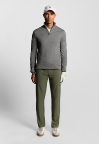 Maglione grigio con zip, pantaloni verde oliva, cappellino bianco con logo, scarpe da golf beige e guanto bianco; abbigliamento da golf semplice e funzionale.