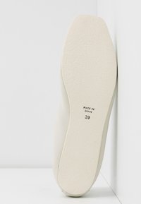 Semelle d'une chaussure blanche avec une surface texturée, étiquetée "Made in Spain" et taille 39, positionnée contre un mur et un sol blancs.