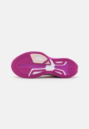 Semelle d'une chaussure de sport rose et blanche montrant un motif de bande de roulement texturé et le logo Adidas sur un fond blanc uni.