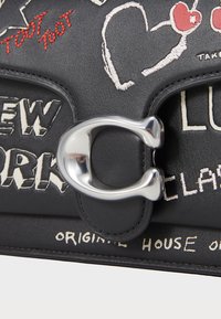 Sac en cuir noir avec quincaillerie en acier inoxydable, motifs brodés et éléments textuels en blanc et rouge, mettant en avant un style graphique moderne.