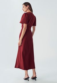 Robe midi bourgogne avec des manches bouffantes courtes, taille cintrée et texture lisse. Associée à des talons noirs à bout ouvert et à des accessoires minimalistes.