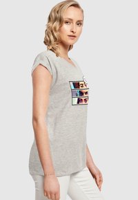 Grå bomulds t-shirt med korte ærmer, der har et farverigt grafisk print af ansigtter på fronten. Rund halsudskæring og afslappet pasform.