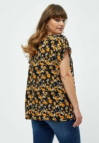 Sort kortærmet top med orange og hvid blomstermønster, der har en løs pasform og rund halsudskæring. Bæres med blå jeans.