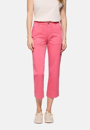 Mujer vistiendo pantalones rosa de cintura alta y corte cropped con bolsillos delanteros de parche, top blanco sin mangas y zapatos casuales beige.