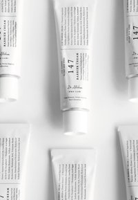 Hvit tube med "147 Barrier Cream" med teksturert mat utførelse. Svart tekst beskriver ingredienser og bruk. Skrukork, minimalistisk design.