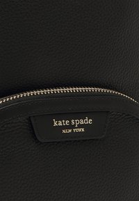 Crna kožna torba s teksturiranim završetkom, zlatnim zatvaranjem na zip i logotipom s natpisom "kate spade NEW YORK."