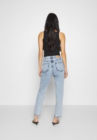 Hög midja blå denimjeans med smal ben, med bakfickor och ljus tvätt. Kombineras med en svart ärmlös topp och sandaler.