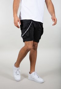 Mustat cargo-shorts, joissa on useita taskuja, sivuvetoketju ja koristeellinen vyö. Yhdistetty valkoisiin Nike Air Force 1 -tennareihin.