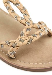 Sandalias trenzadas en color moreno con gemas claras decorativas, suela plana y una suave plantilla de ante, con diseño de correas cruzadas y costuras detalladas.