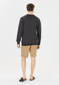 Sweatshirt gris avec des manches raglan, en coton, avec des poignets côtelés, associé à un short beige. Le modèle porte des chaussures noires à enfiler.