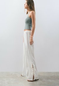 Pantalones anchos ligeros de color blanco con detalles de encaje y lazos laterales, combinados con una camiseta de tirantes ajustada de canalé en azul grisáceo claro.