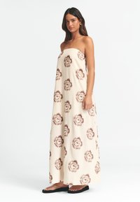 Triipuvaba maksikleit beežist kangast pruunide lillemusteritega, millel on lõdva istuvuse ja voolava disainiga, ning lame mustade talladega sandaalid.