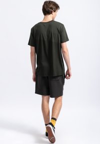 Donkergroene T-shirt met korte mouwen en een ronde hals, gecombineerd met donkere shorts met zijzakken en een gestructureerde stof.