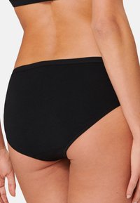 Mutande hipster in cotone nero con un cinturino senza cuciture e una texture liscia, progettate per il comfort e la minima visibilità sotto i vestiti.